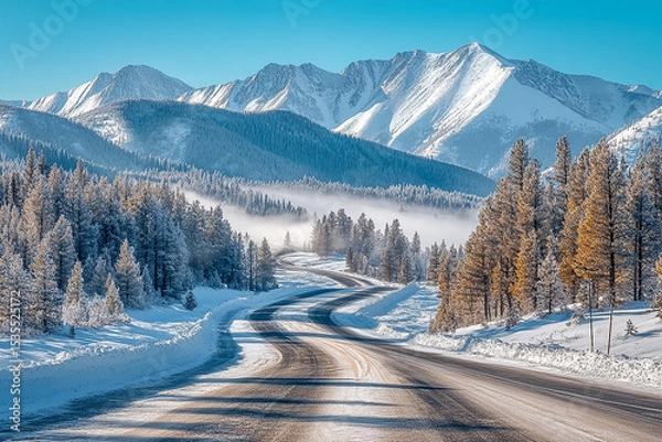 Obraz Winding asphalt road through a snow covered forest with mountains in the back