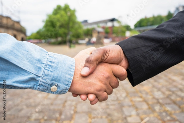Obraz Handshake between two individuals in a public outdoor setting showcasing cooperation and agreement during daytime in an urban environment