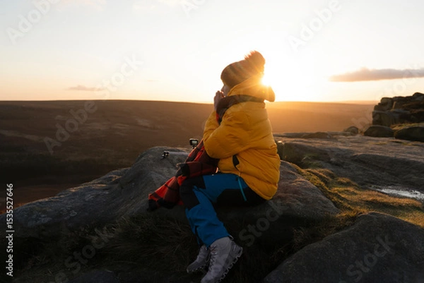 Obraz Sunset contemplation on a rocky outcrop in a vibrant yellow jacket during a cool evening in a serene landscape