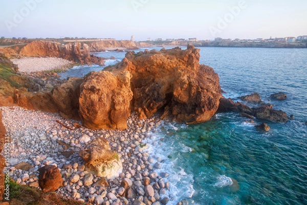 Fototapeta Sunny rocky coastline of Atlantic Ocean in the rays of setting sun, Papoa Island, Peniche, Portugal