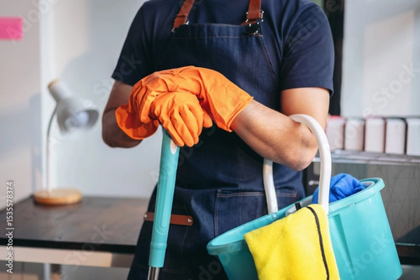 Obraz Housekeeping and cleaning concept, Happy young man in orange rubber gloves wiping dust using mop while cleaning on floor at home