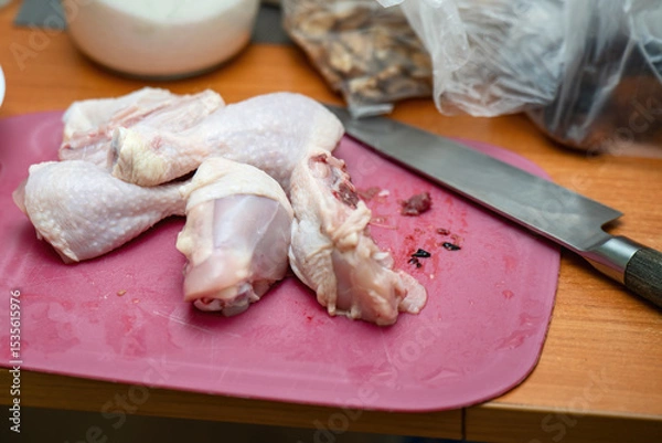 Fototapeta Chopped chicken drumsticks on a plastic cutting board with a knife nearby, ready for cooking preparation
