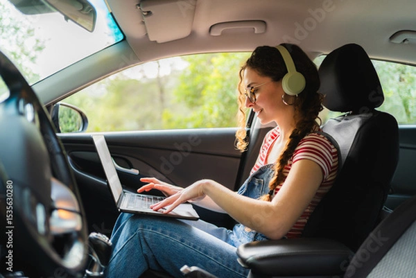 Fototapeta Freelancer working remotely from her car using laptop and headphones