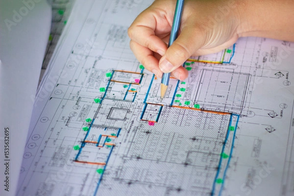 Fototapeta Civil Engineer Reviewing Detailed Building Layout with Hand on Blueprint