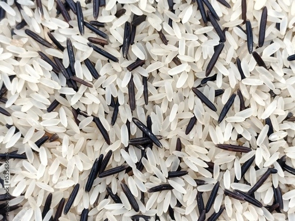 Fototapeta Background view of a mix of uncooked parboiled long-grain rice and wild rice, showcasing a contrast between light beige and dark brown grains.