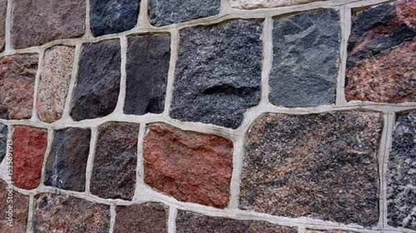 Fototapeta Close-up view of a multicolored stone wall with irregular rectangular blocks and white grout. The textured surface and natural colors give a rustic and architectural feel.