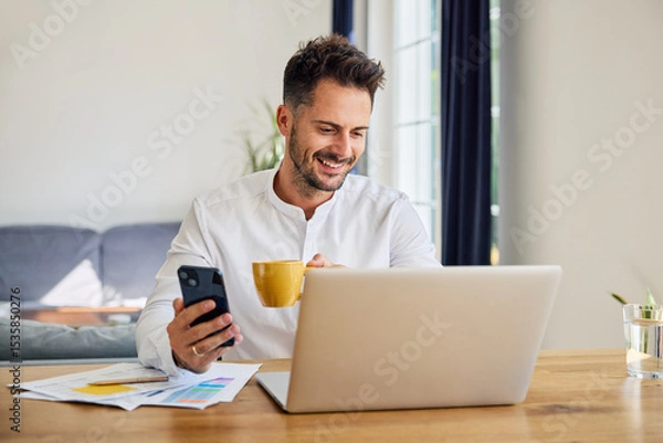 Fototapeta Man using laptop and mobile phone while working from home