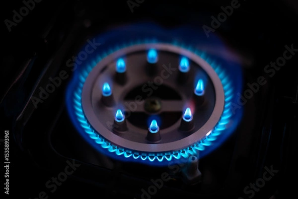 Fototapeta Close-up of a lit gas burner with blue flames in a dark setting, showing energy, heat, and kitchen technology with a focus on fire safety and home cooking