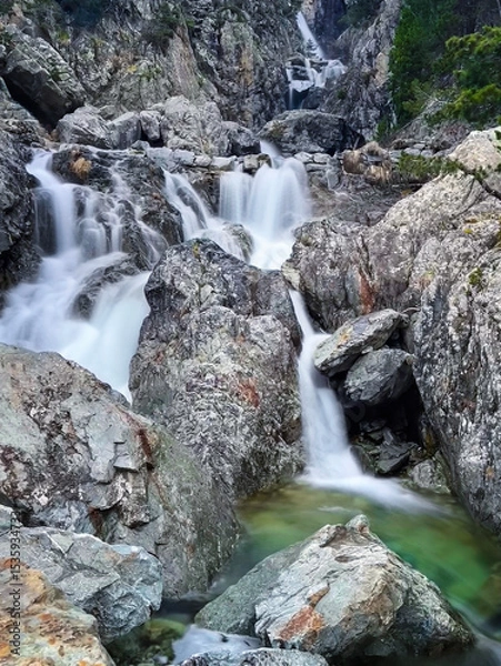 Fototapeta mountain stream winding through a rocky canyon, creating a stunning sequence of crystal-clear waterfalls and serene natural beauty