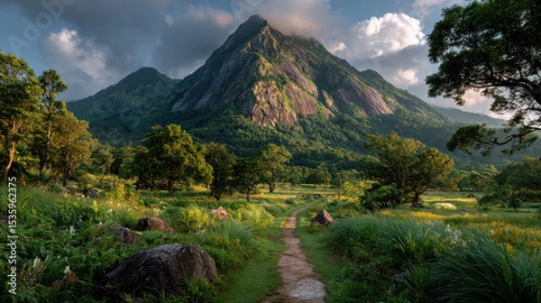 Fototapeta Sustainable path to success is shown by winding trail leading through lush green fields toward majestic mountain under dramatic sky.