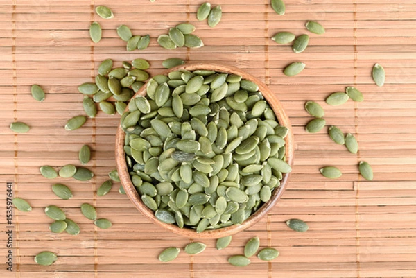Obraz Top view of peeled pumpkin seeds in wooden bowl and on mat.
