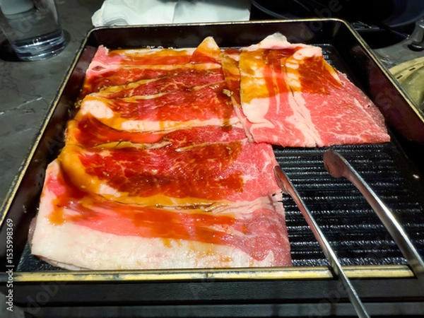 Fototapeta Close up of thinly sliced raw fatty beef meat in tray next to a Japan BBQ style gas grill