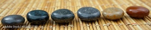 Fototapeta Polished stones arranged on a woven bamboo mat, ready for spa use , natural, beauty, calm
