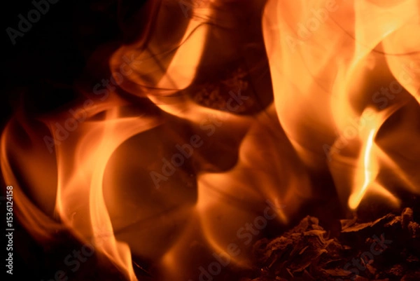 Fototapeta Close-up image of bright orange flames against a backdrop of black ash and burnt debris. A strong visual composition depicting the power, energy, and beauty of nature in the form of the fire element. 