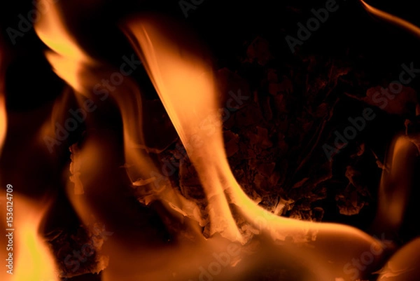 Fototapeta Close-up image of bright orange flames against a backdrop of black ash and burnt debris. A strong visual composition depicting the power, energy, and beauty of nature in the form of the fire element. 