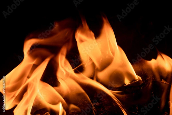 Fototapeta Close-up image of bright orange flames against a backdrop of black ash and burnt debris. A strong visual composition depicting the power, energy, and beauty of nature in the form of the fire element. 