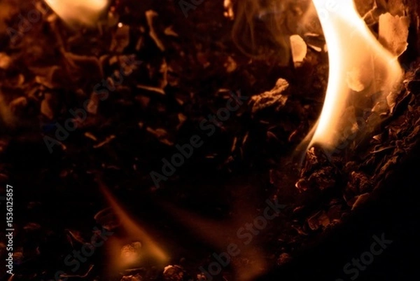 Fototapeta Close-up image of bright orange flames against a backdrop of black ash and burnt debris. A strong visual composition depicting the power, energy, and beauty of nature in the form of the fire element. 