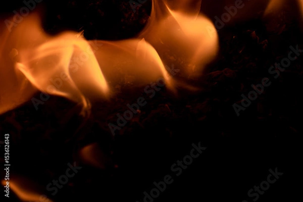 Fototapeta Close-up image of bright orange flames against a backdrop of black ash and burnt debris. A strong visual composition depicting the power, energy, and beauty of nature in the form of the fire element. 