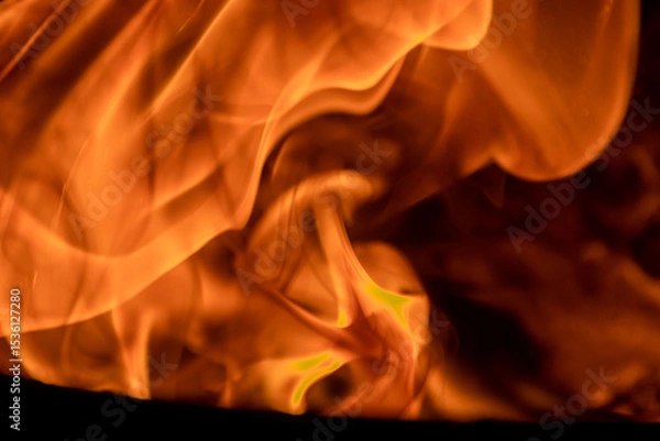 Fototapeta Close-up image of bright orange flames against a backdrop of black ash and burnt debris. A strong visual composition depicting the power, energy, and beauty of nature in the form of the fire element. 