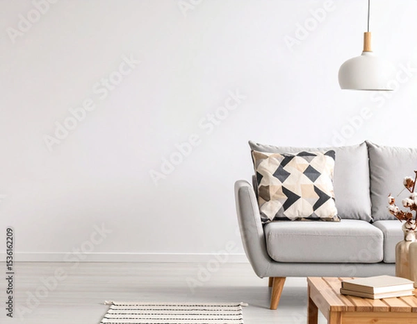 Fototapeta Modern Living Room Interior: A cozy and stylish living room features a light grey sofa adorned with geometric patterned cushions, a wooden coffee table with books, a simple pendant lamp.