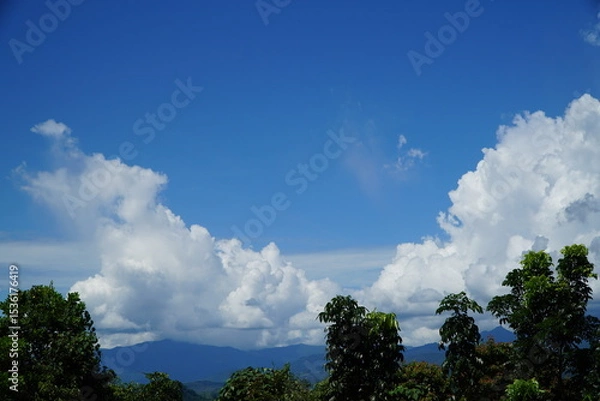 Fototapeta Vast expanse of a clear blue sky, dotted with fluffy white clouds, over a lush green mountain range.
