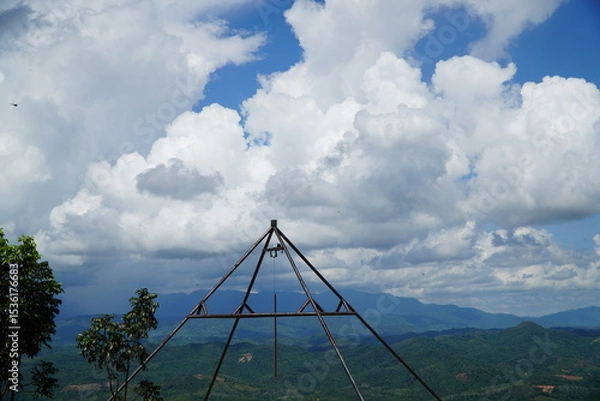 Fototapeta Metal structure atop a hill overlooking a lush green landscape with a cloudy sky.