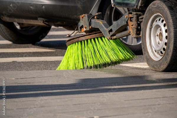 Obraz Street sweeper machine actively cleaning road surface with rotating brushes. Bright green bristles efficiently removing debris from pavement in urban setting, enhancing cleanliness and safety.