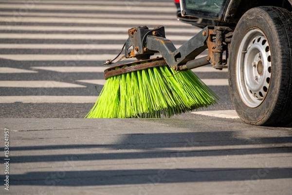 Obraz Street sweeper machine actively cleaning road surface with rotating brushes. Bright green bristles efficiently removing debris from pavement in urban setting, enhancing cleanliness and safety.