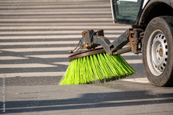 Obraz Street sweeper machine actively cleaning road surface with rotating brushes. Bright green bristles efficiently removing debris from pavement in urban setting, enhancing cleanliness and safety.