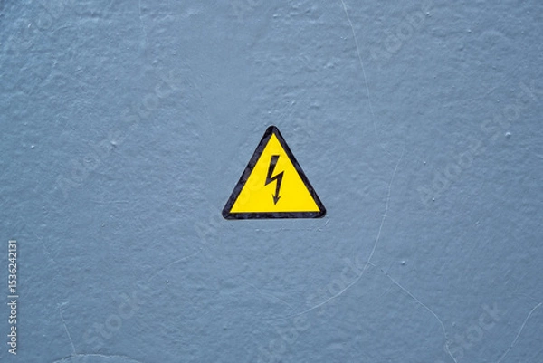 Obraz Yellow caution sign with high voltage warning symbol against a gray background. Indicates electrical danger and promotes safety awareness in hazardous areas, essential for protection.