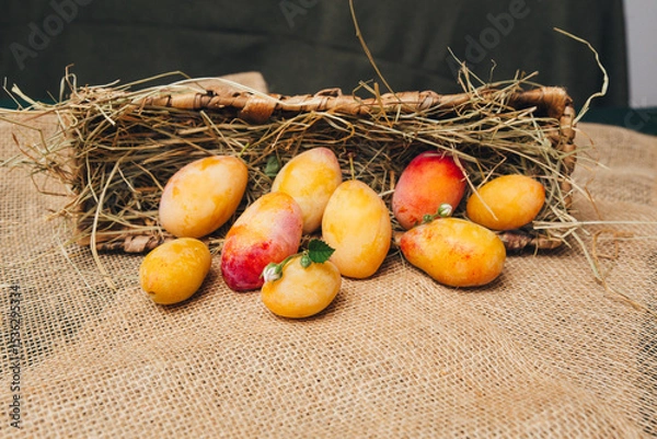 Fototapeta Still life with yellow plums in a basket, located on a light wooden surface, minimalism and naturalness.