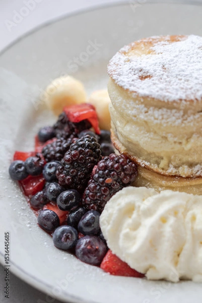 Obraz Close-up of fluffy Japanese souffle pancakes dusted with powdered sugar, served with fresh blackberries, blueberries, strawberries, vanilla ice cream, and whipped cream on white plate Delicious brunch