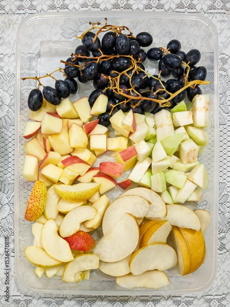 Fototapeta Top view of seeded black grapes, sliced red apples, guava, and pear in a transparent plastic container. Colorful fresh fruit mix, healthy snack, natural ingredients, clean eating