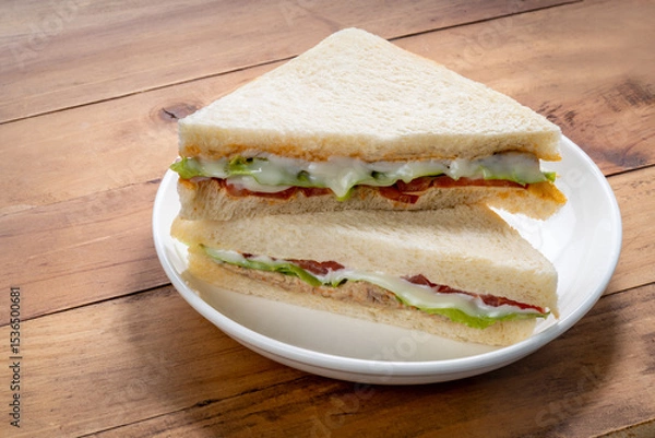 Obraz Sandwich with fresh vegetables and creamy salad dressing on a white plate on wooden background.