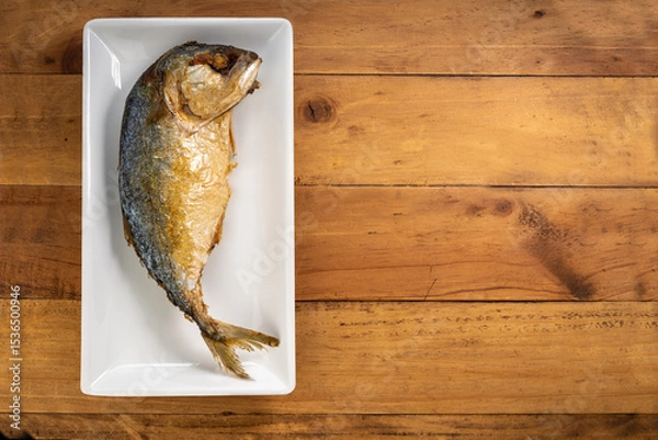 Obraz Fried mackerel on a white plate placed on a wooden surface,Traditional Thai Golden-brown fried fish (mackerel) on a white plate on wood surface.