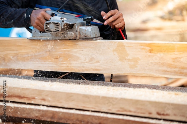 Fototapeta Male carpenter hand using an electric planer on wooden plank at construction site. Woodworker planing timber in his workshop with sawdust spreading around. Lumber industry and carpentry work tool