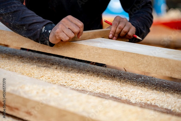Fototapeta Male carpenter hand placing a piece of wood and use pencil to draw a line for cutting wooden plank in workshop. Wood measuring and shaving process for lumber industry