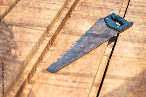 Fototapeta Rustic old hand saw on timber stack at construction site. Work tool for cutting in lumber industry