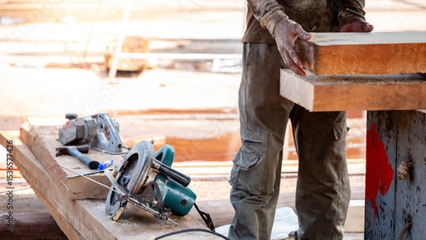 Fototapeta Male carpenter setting workbench preparing work tools for cutting and planing timber. Electric circular saw with planer and hammer on wooden plank at construction site. Lumber industry concept
