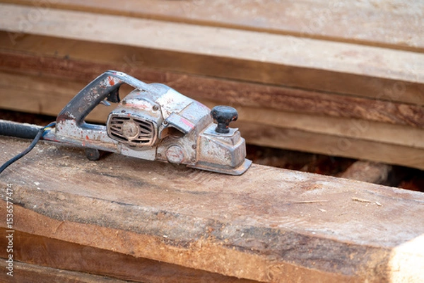 Fototapeta Rustic old electric planer on timber stack or wooden plank with sawdust spreading around. Work tool for carpentry. Lumber industry concept
