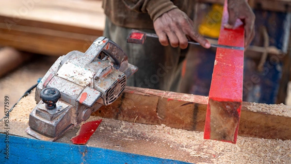 Fototapeta Rustic electric planer on workbench with carpenter hand squaring timber behind. Woodworker planing wooden plank at construction site. Carpentry work tool and lumber industry concept