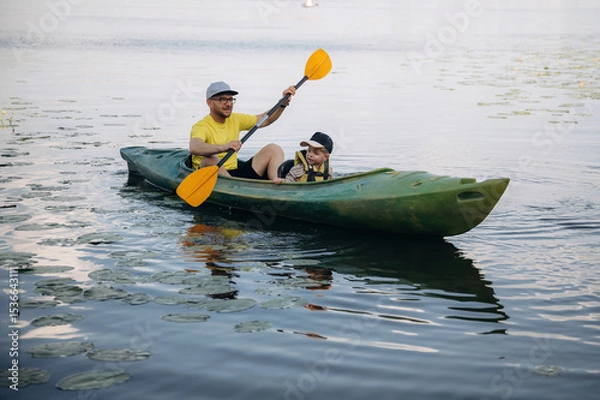 Fototapeta Sportive father is with his young son is swimming in the kayak