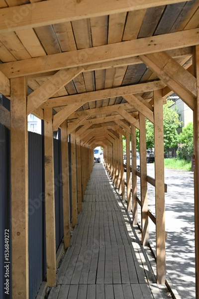 Fototapeta Long wooden walkway under construction canopy in urban area with greenery in the background