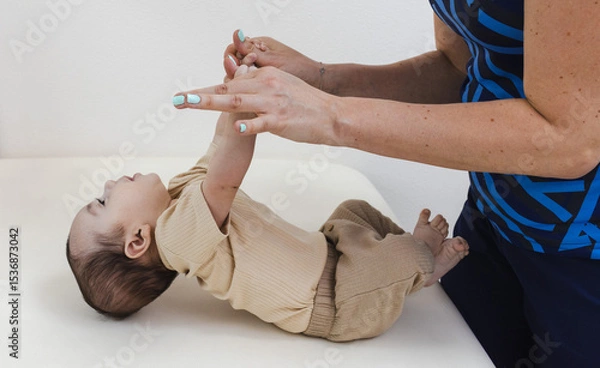 Fototapeta Physical therapist working with infant during neurological pediatric exam for test on newborn reflexes. Pull to sit or arm traction test