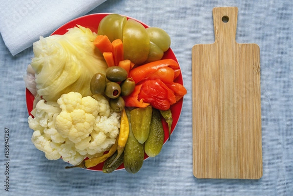 Fototapeta Balkan cuisine. Torshi , mix of different pickled vegetables , in  red plate. Cutting board, copy space