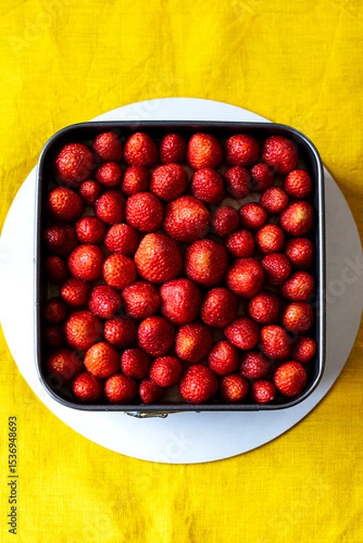 Fototapeta Fresh strawberry in a square springform pan on white round support, yellow tablecloth background.