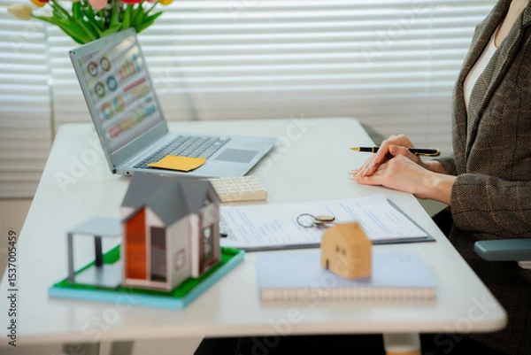 Fototapeta Asian real estate agent in modern office consulting with client, showing property using laptop, mortgage business with house plans, calculator and documents, mortgage and real estate