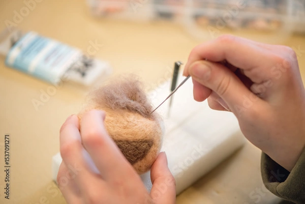 Fototapeta Close-up of artist hands using needle felting technique attaching small piece of wool on handmade toy figure, crafting process of creating cute animal from natural materials