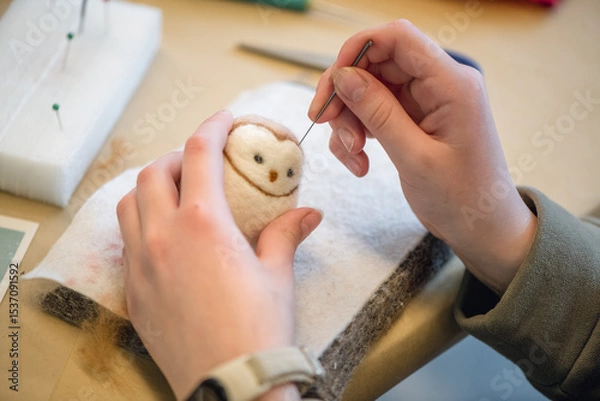 Fototapeta Close-up of artist's hands using a special needle to create a needle felted animal toy from wool roving, demonstrating the delicate process of needle felting
