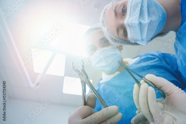 Fototapeta dentist surgeon holding teeth for tooth extraction with assistant leaning and looking at patient.  Medical team performing surgery